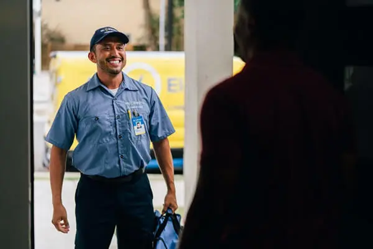  A Smiling Mr. Electric Electrician Stands in Front of an Open Door Holding a Bag While a Man Inside the Doorway Looks at Him