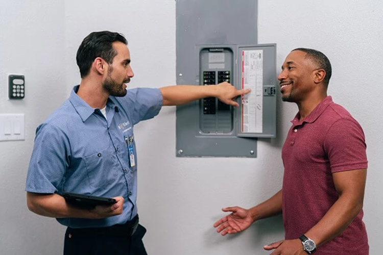 A Mr. Electric Service Professional Holding a Tablet Points at an Open Electrical Panel While Talking to a Smiling Man