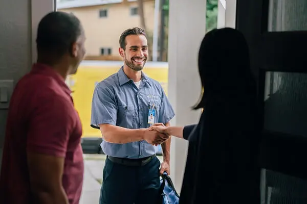 A Man and Woman Pictured from Behind in an Open Doorway and the Woman Shaking Hands with a Mr. Electric Electrician Outside