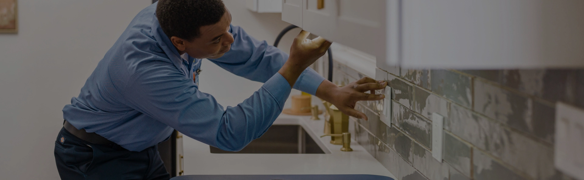 A Mr. Electric Electrician Stands at a Counter with Tools Spread Out on it and Uses a Device to Test an Electrical Outlet